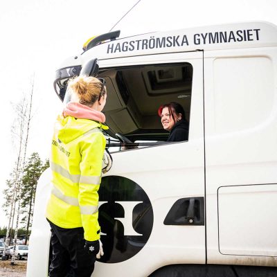 En lärare ler mot en elev som kör lastbil.